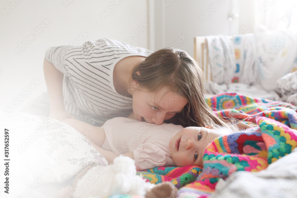 Young beautiful woman playing with her baby child in bedroom