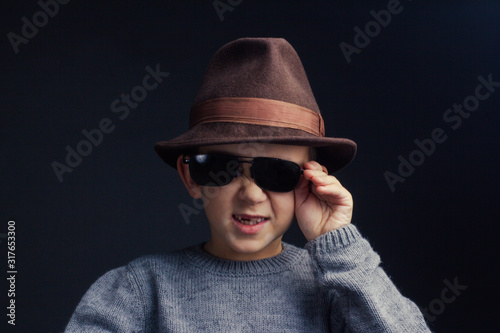 Studio portrait of a boy in a grey sweater, brown hat and sunglasses