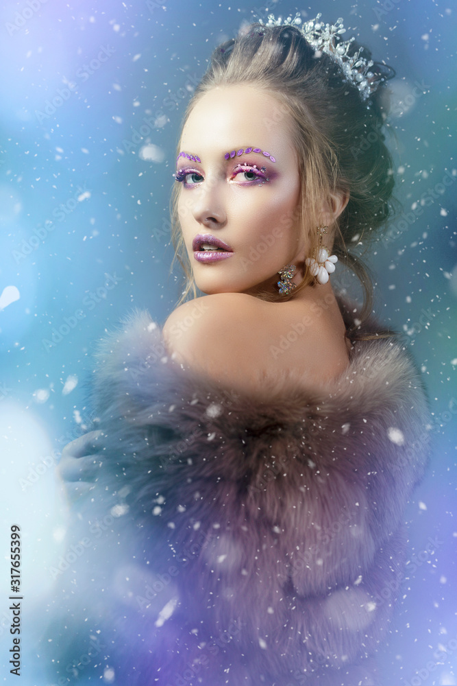 The Snow Queen. Winter girl in a fur coat showered with snow. Model with beautiful makeup on a snowy background. The Snow Queen. Winter girl in a fur coat showered with snow. Model with beautiful makeup on a snowy background.