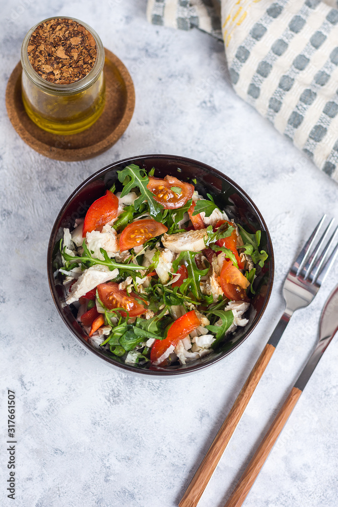 Salad with chicken, tomatoes and spinach with Beijing cabbage in a dark bowl with a napkin, butter and devices on a light background Salad with chicken, tomatoes and spinach with Beijing cabbage in a dark bowl with a napkin, butter and devices on a light background
