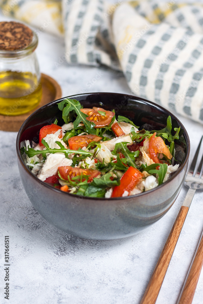 Salad with chicken, tomatoes and spinach with Beijing cabbage in a dark bowl with a napkin, butter and devices on a light background Salad with chicken, tomatoes and spinach with Beijing cabbage in a dark bowl with a napkin, butter and devices on a light background