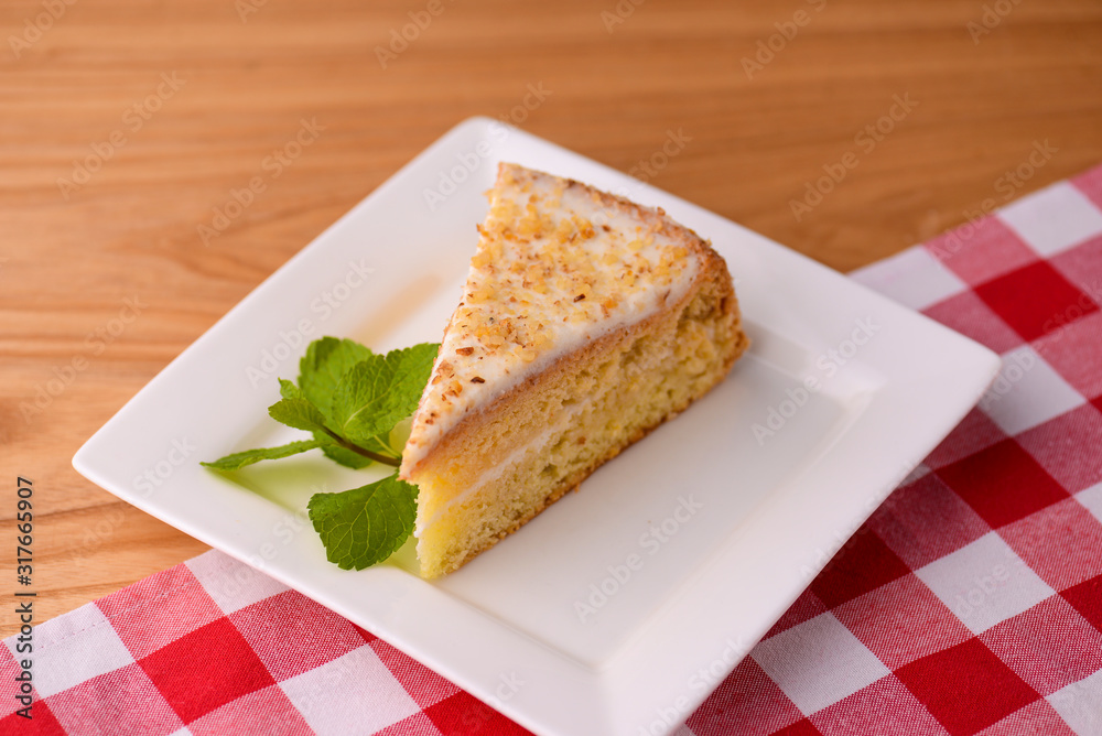 Slice of victoria sponge cake with cream filling, served with a mint leaf on a white plate on light wooden table Slice of victoria sponge cake with cream filling, served with a mint leaf on a white plate on light wooden table