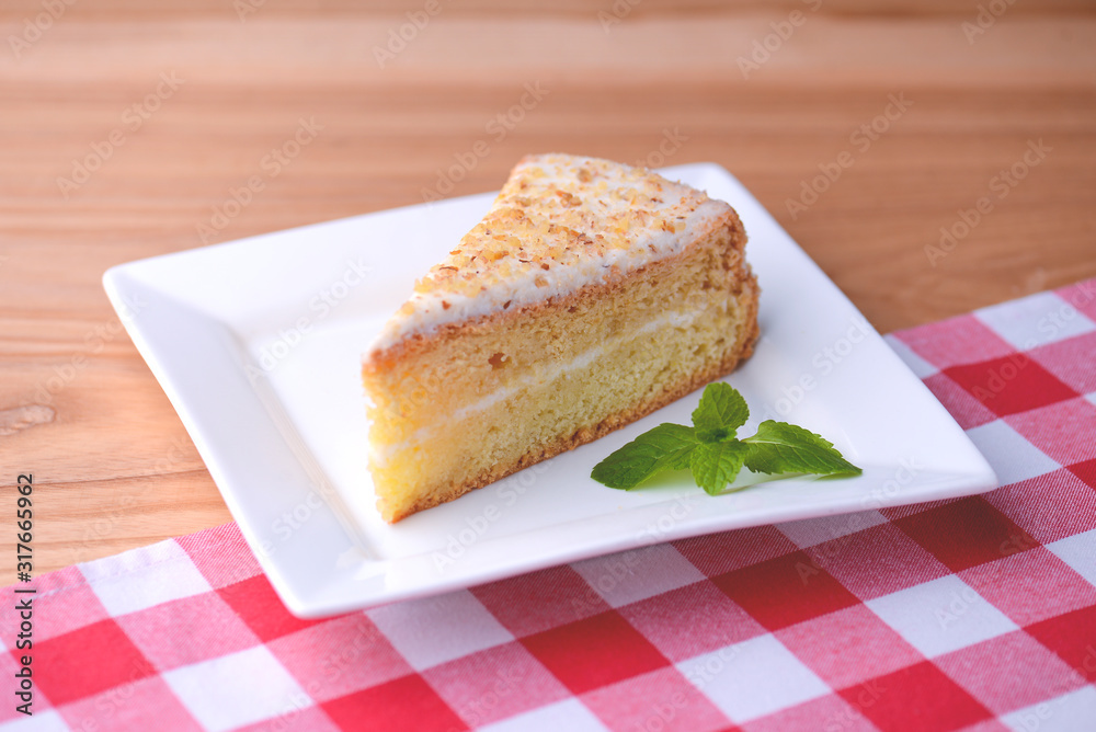 Slice of victoria sponge cake with cream filling, served with a mint leaf on a white plate on light wooden table Slice of victoria sponge cake with cream filling, served with a mint leaf on a white plate on light wooden table