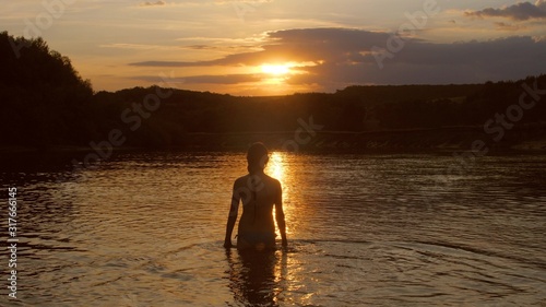 girl goes into the water at sunset fiery sun. young woman bathes in the evening in the river. rest by the water.