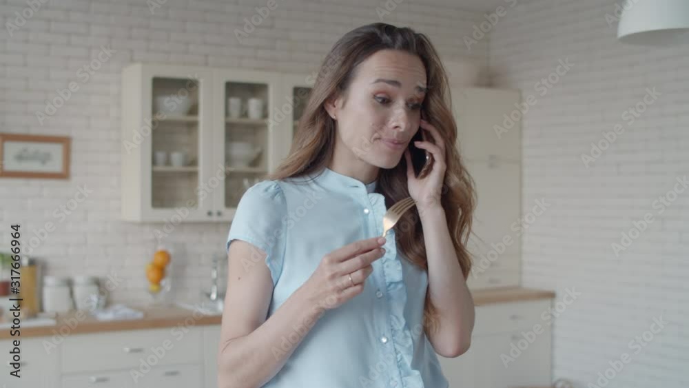 Young businesswoman talking mobile phone in white kitchen interior. Young businesswoman talking mobile phone in white kitchen interior.