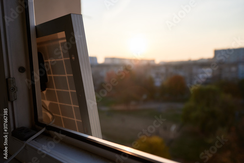 View from inside at solar battery standing on the window of a high-rise residential building. Outside the window, sunset in the sleeping area of the city in the evening