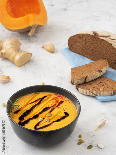 Pumpkin cream soup with balsamil souse and olive oil. Decorated rosemary branсh and pumpkin seeds. Traditional ingredients, healthy food concept. Blue napkin, gray stone background, close up