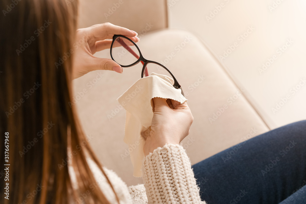 Young woman wiping eyeglasses at home, closeup - obrazy, fototapety, plakaty 