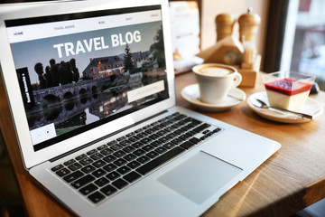 Laptop with open page of travel blog on table in cafe