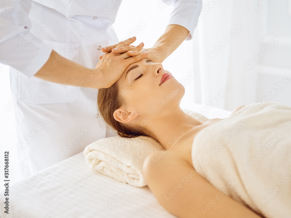 Beautiful woman enjoying facial massage with closed eyes in spa center. Relaxing treatment concept in medicine