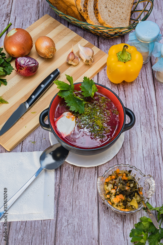 Red borsch, a national dish of Ukrainian cuisine. In the photo, borsch is a black ceramic with sour cream, green onions and garlic on a wooden background. Red borsch, a national dish of Ukrainian cuisine. In the photo, borsch is a black ceramic with sour cream, green onions and garlic on a wooden background.