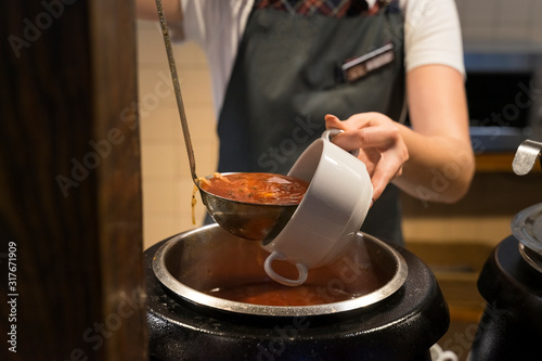 the cook pours borsch in a plate from a large tank