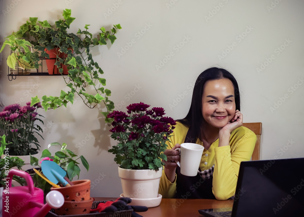 Asian female gardener sitting in her plant workshop drinking coffee and working online on computer laptop  .start up business,gardening.