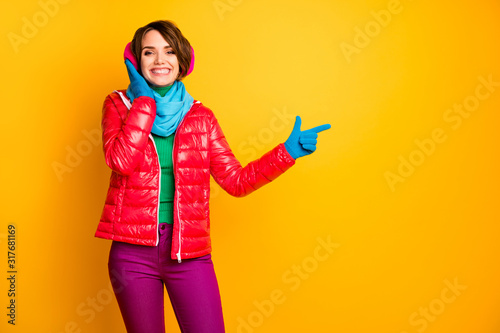 Photo of pretty lady directing fingers empty space touch stylish modern pink earmuffs wear casual red coat blue scarf gloves ear covers pants isolated yellow color background