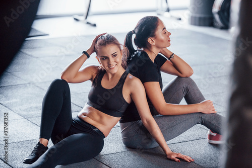 Two young girls in sportive clothes sitting in the gym together at daytime