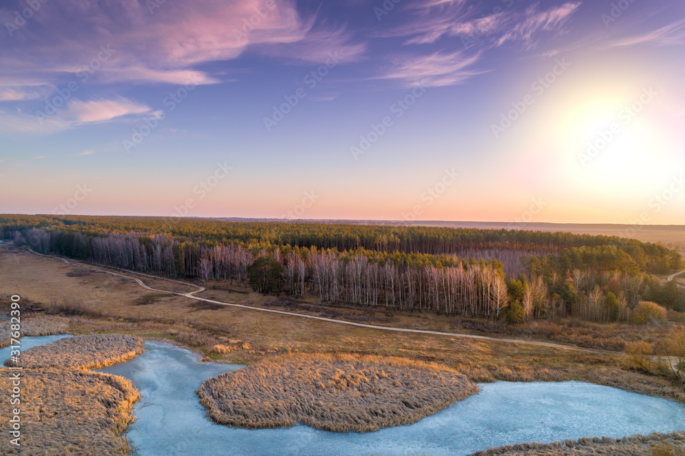Aerial view of countryside and frozen brook in evening at sunset light. Beautiful nature landscape with cloudy sky.