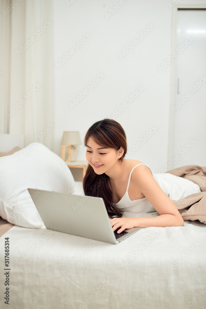 Smiling Asian young woman using laptop in bed at home Smiling Asian young woman using laptop in bed at home