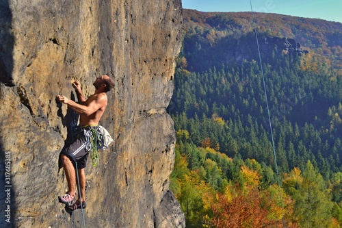 Young man is climbing on the sandstone rock in Sachsen Switzerland. Beautiful autumn day in Germany.