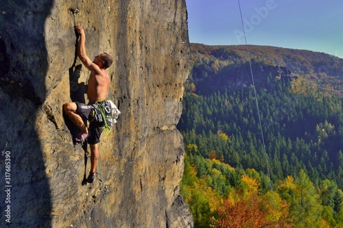 Young man is climbing on the sandstone rock in Sachsen Switzerland. Beautiful autumn day in Germany.