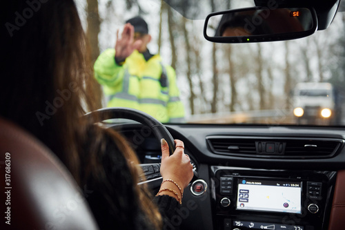 Fotografie Male police officer in green uniform stops vehicle with female driver on the roa