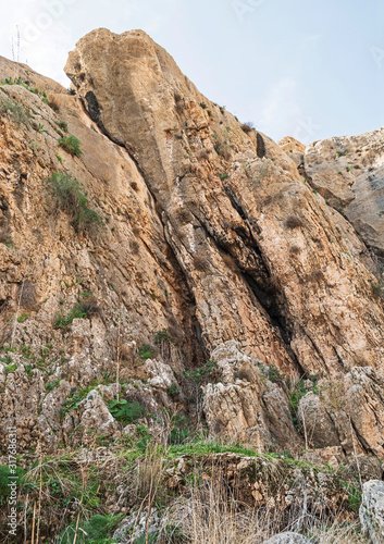 tilted limestone rock formation near ein prat in wadi qelt in the west bank with plants in the crevices and the ruins of an ancient aqueduct in the foreground