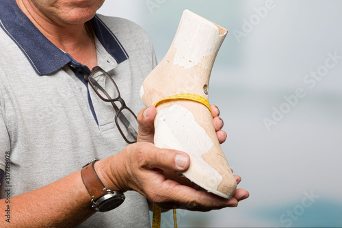 hands of a orthopedic shoemaker is checking an individual crafted wooden last