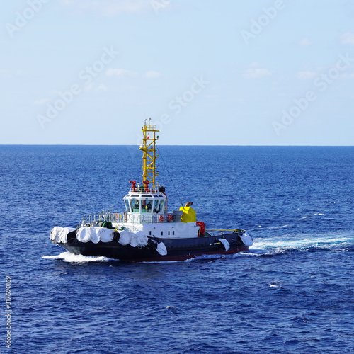 A bright, powerful industrial tugboat cuts through the sea waves on a sunny day. mole tugboat floating in the blue water of the Pacific Ocean pushing a big wave
