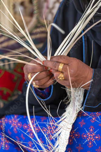 Emirati woman is weaving traditional basket from palm leaves, hands in frame