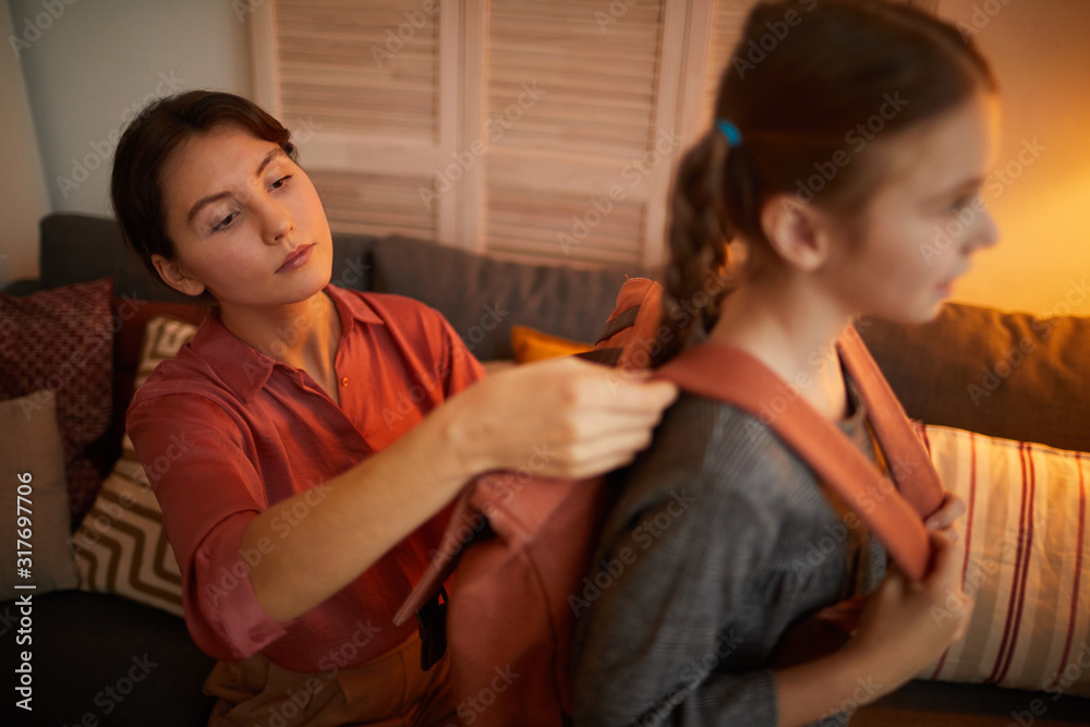 Young mother collecting her daughter to school she putting on the backpack on her back in the living room at home Young mother collecting her daughter to school she putting on the backpack on her back in the living room at home