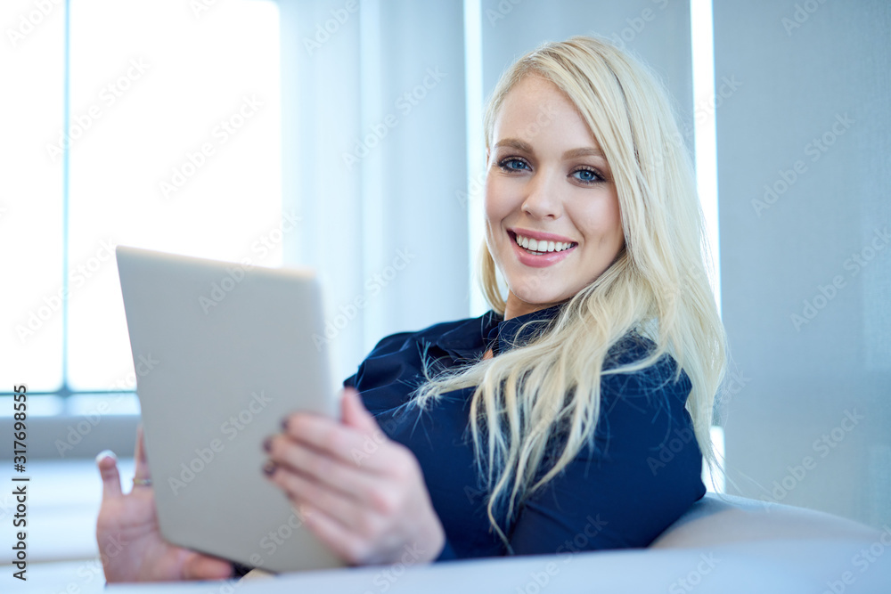Portrait of a smiling young businesswoman sitting on a sofa in a modern office working online with a digital tablet Portrait of a smiling young businesswoman sitting on a sofa in a modern office working online with a digital tablet