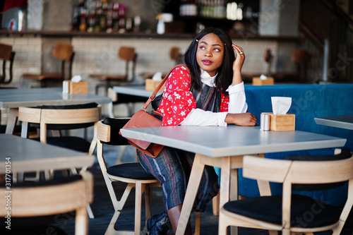 Сonfident young african american woman in smart casual wear with handbag at cafe.