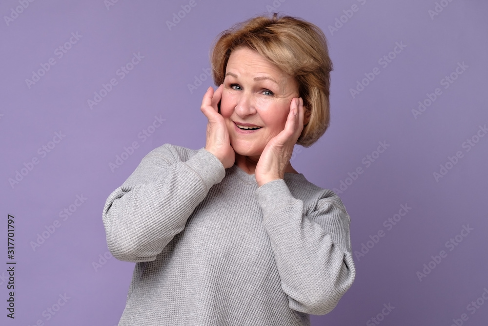 Old pretty woman with surprised expression on her face. Studio shot on violet wall. Old pretty woman with surprised expression on her face. Studio shot on violet wall.