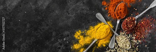 Obraz  z motywem A banner with spices in metal spoons on a black table. Space for text