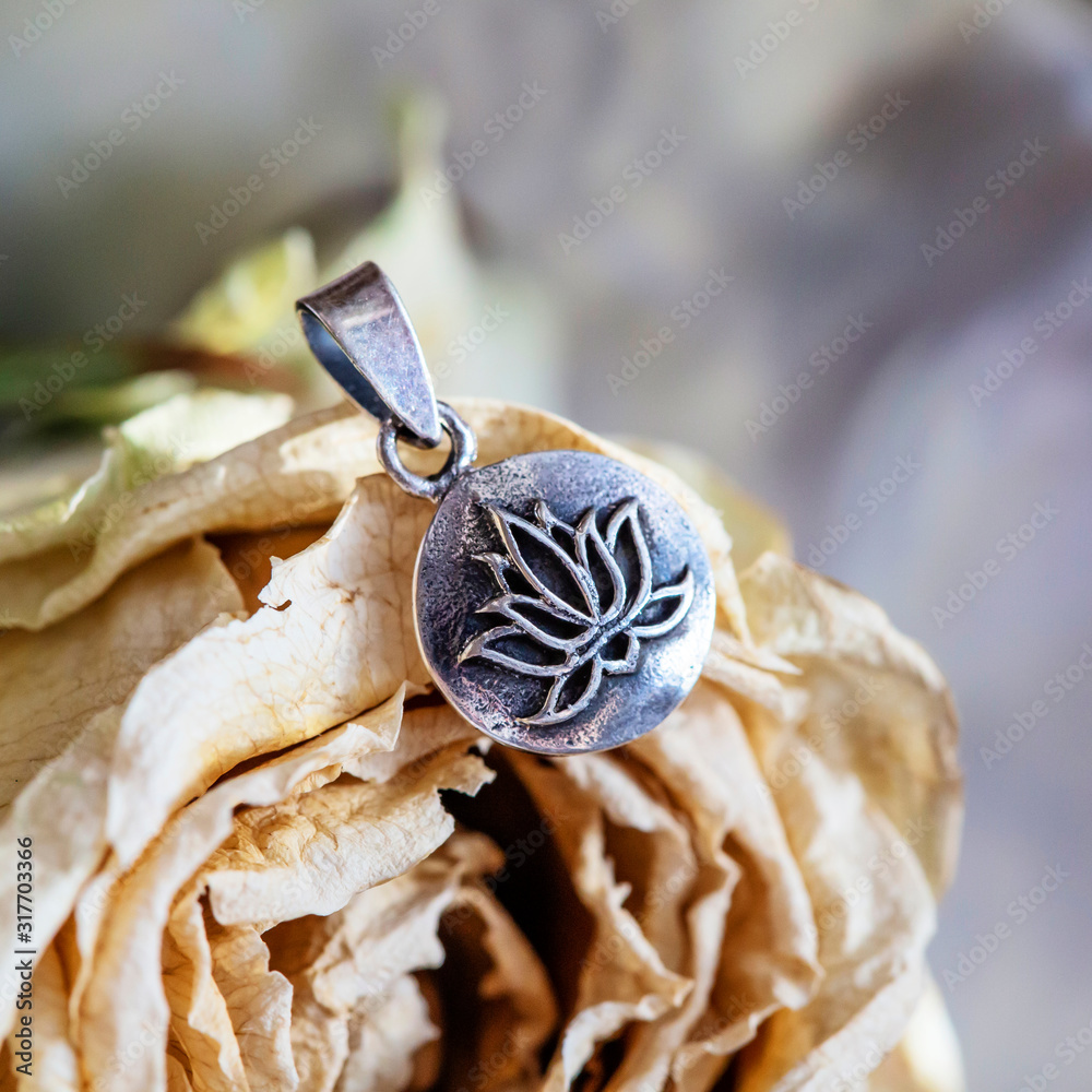 Silver pendant with lotus blossom shape in madala round metal disc, dry rose background Silver pendant with lotus blossom shape in madala round metal disc, dry rose background
