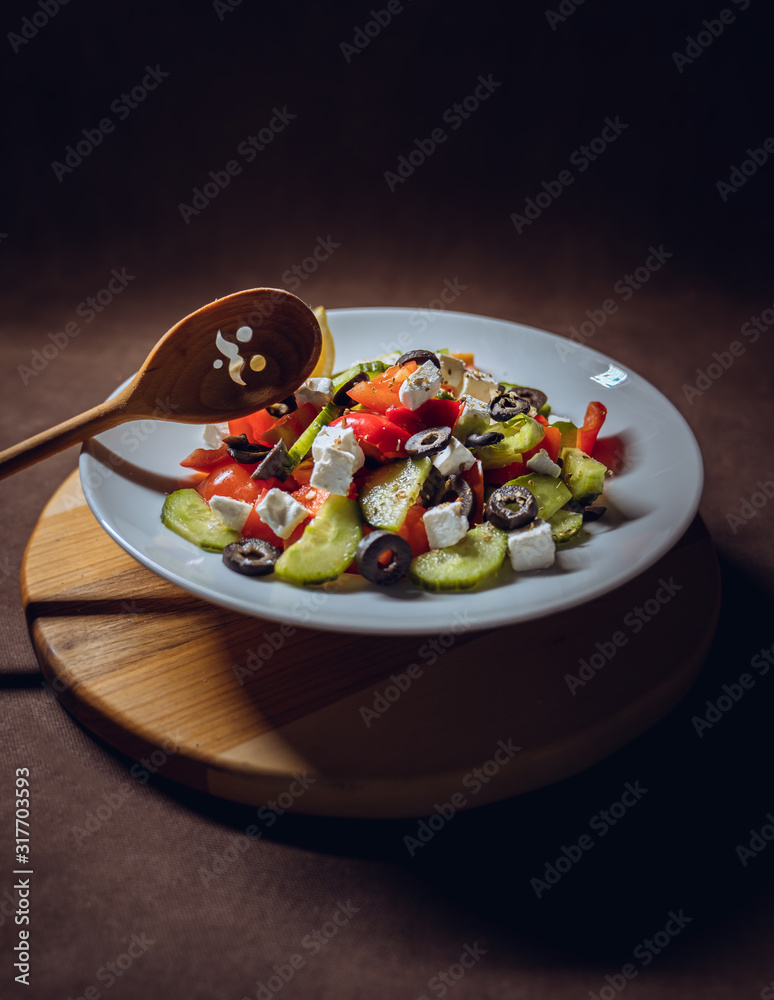 Salad with tomato, cucumber, cheese, olives, basil, spices, pepper with wooden face sculpture spoon and bread