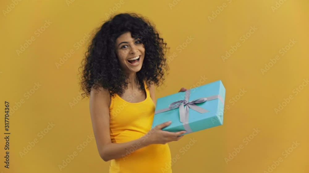happy bi-racial pregnant woman taking gift box isolated on dark yellow happy bi-racial pregnant woman taking gift box isolated on dark yellow