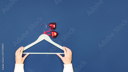 Female hands holding empty coat hanger with two red glass heart pendants. Flat lay on dark blue. 14 February. love and feelings St Valentine's Day Card celebration concept or sale with copy space