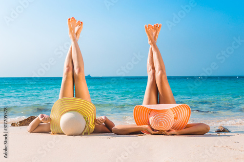 Fototapeta Naklejka Na Ścianę i Meble -  Young beautiful women wearing bikini lying sunbathing with legs crossed and raised up pointing to the sky.relaxing on beach on a sunny day, Vacation concept