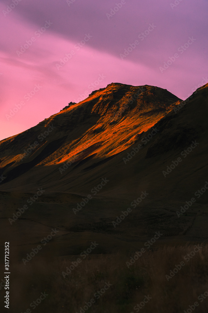 Beautiful scenic sunset in Iceland. Yellow lit mountain side with pink clouds.