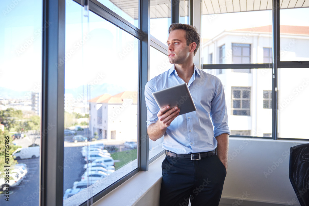 Fototapeta premium Young businessman looking out window while holding digital tablet