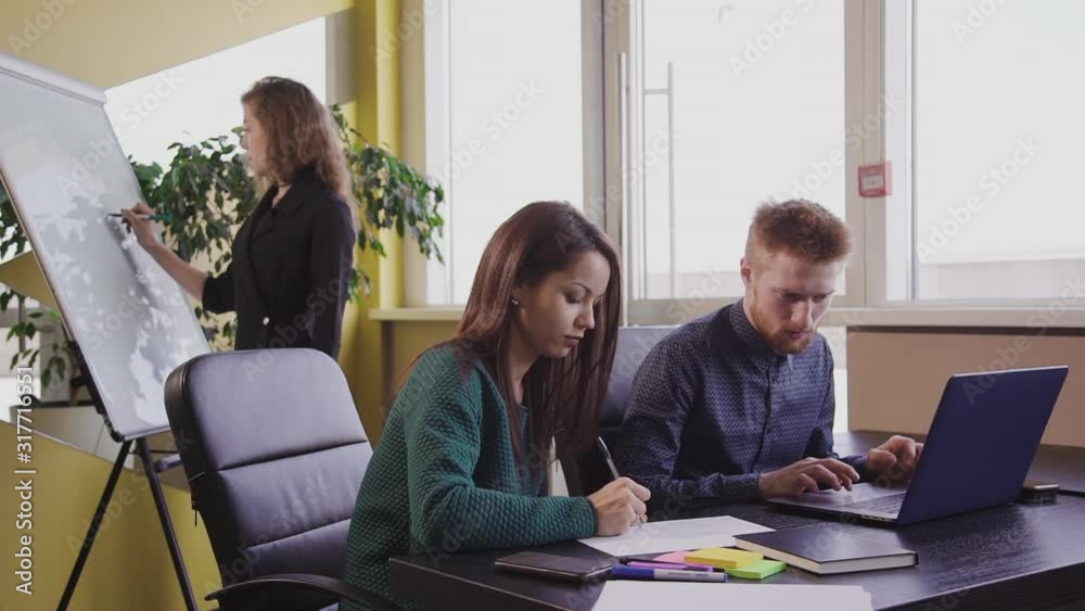 Group of american specialists work at table with laptop in ofice room. Businesspeople at desk. Beautiful woman coach write on whiteboard. Group of american specialists work at table with laptop in ofice room. Businesspeople at desk. Beautiful woman coach write on whiteboard.