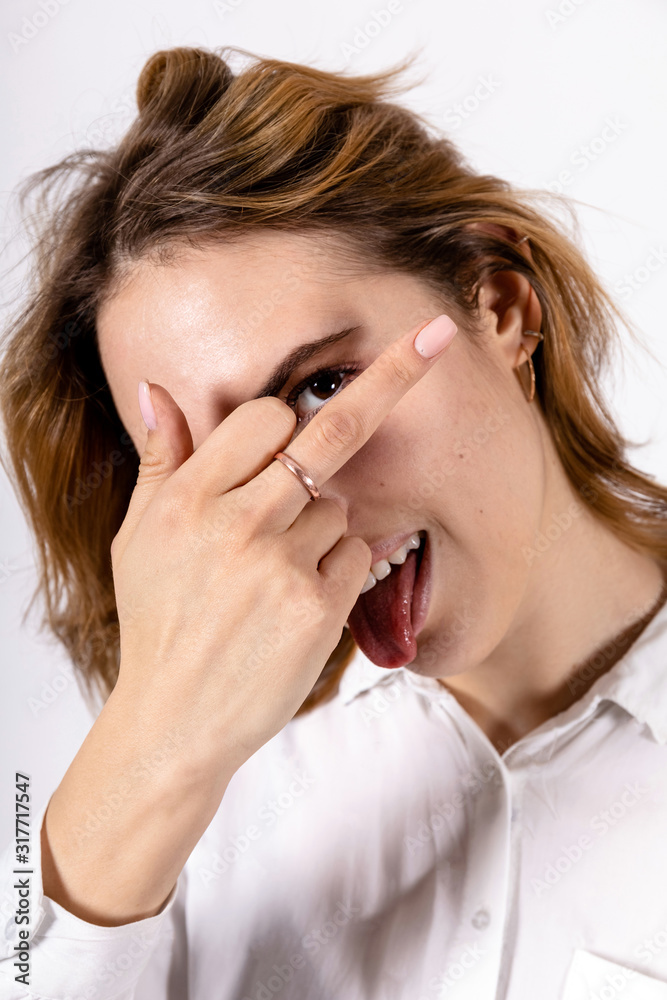 young smiling girl in a white shirt with a sticking out tongue showing fuck off sign to the camera on a white background young smiling girl in a white shirt with a sticking out tongue showing fuck off sign to the camera on a white background