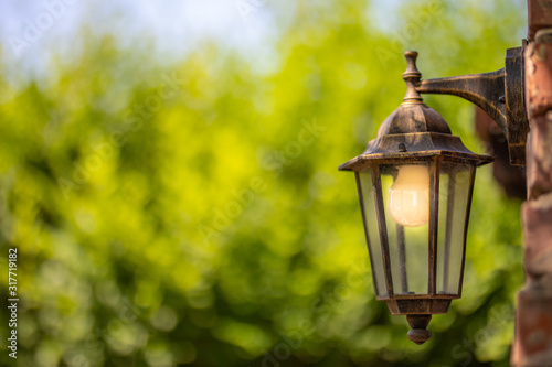 Old electrical lamp on the brick wall that illuminates on blurred sunset nature background