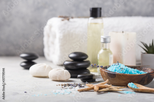 Beauty still life of massage oil bottle of aroma essential and natural fragrance salt with stones, candles on concrete grey table. Composition of spa treatment