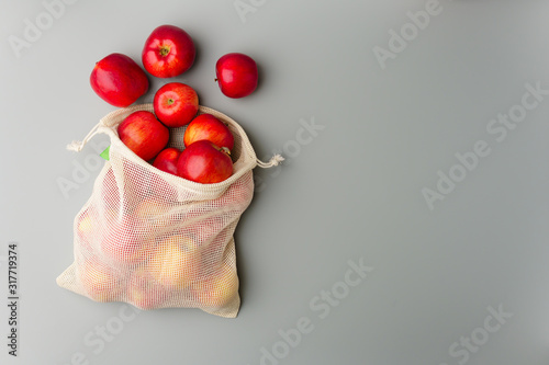 Red apples in a reusable cotton bag on a gray background. photo