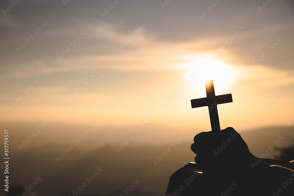 human hands praying to the GOD while holding a crucifix symbol with bright sunbeam.