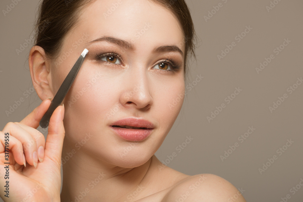 Eyebrow correction. Closeup of a beautiful young woman. plucking eyebrows. Portrait with tweezers near the eyebrows. Beauty concept.