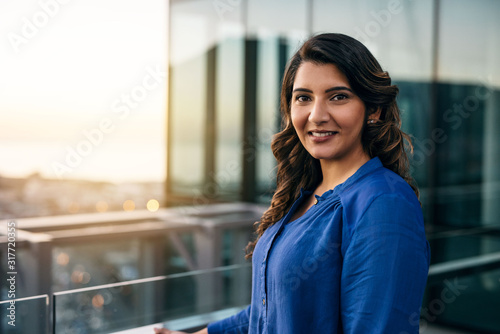 Smiing young businesswoman standing on an office balcony at dusk photo