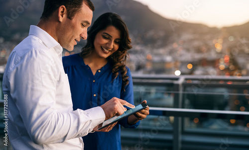 Diverse coworkers standing on an office balcony using a tablet