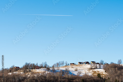 A Plane Crossing the Blue Sky above an Isolated Mountain Village on a Sunny Winter Day